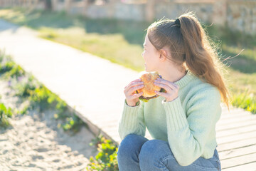 Young pretty girl holding a burger at outdoors in back position