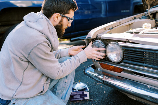 Millennial man replacing headlights in classic station wagon