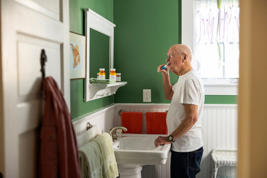 Senior Citizen man brushing teeth at home in green bathroom