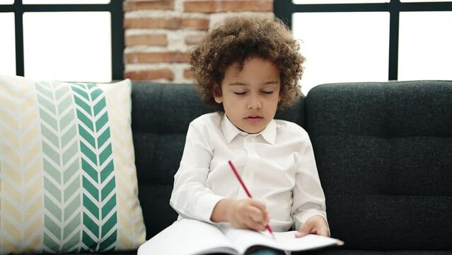 African american boy preschool student sitting on sofa drawing on notebook at home
