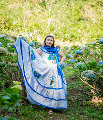 Smiling woman in national folk costume in a field surrounded by flowers. People in Nicaraguan...
