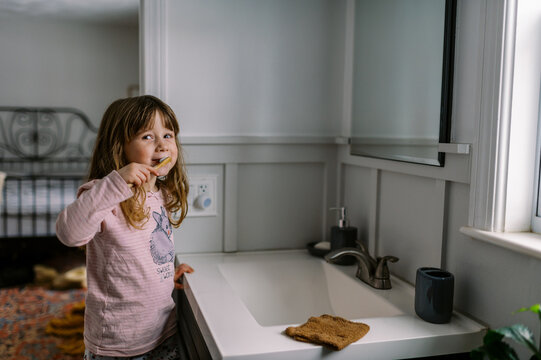 happy toddler girl in bathroom brushing her teeth by herself