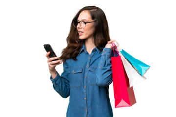 Young caucasian woman over isolated background holding shopping bags and writing a message with her cell phone to a friend