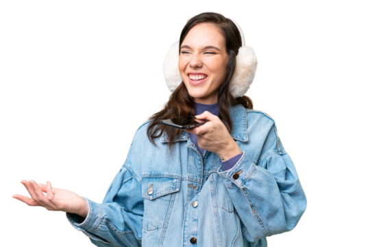 Young caucasian woman wearing winter muffs over isolated background keeping a conversation with the mobile phone with someone