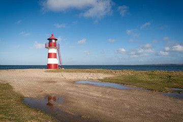 red striped lighthouse on the sandy coast of a fjord in denmark - obrazy, fototapety, plakaty