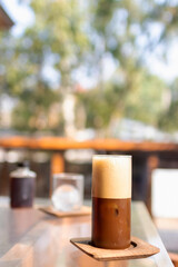 Iced coffee glass on table with soft sunlight on garden background. Espresso mixed with lime juice with sliced lime. 