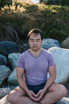 Man with eyes closed meditiating outside on rocks.