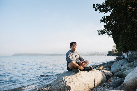 Mindful man meditiating outside on rocks.