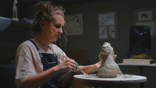 European blonde girl sculptor creates sculpture, statue for interior, bozzetto. The woman has her own local business, a freelancer. The female uses the tools of a sculptor, stecca for clay. - Powered by Adobe