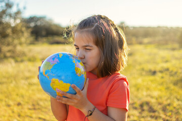 Portrait Of A Beautiful Girl In A Nature Park At Sunset Hugging And Kissing The Globe. Earth Day Concept
