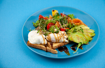 Healthy breakfast. Avocado and salmon, poached egg and toast, salad and vegetables. Microgreens on a plate. Food bowl. Lunch on a blue plate. Sauce and sesame seeds, lemon tomatoes. Top view.