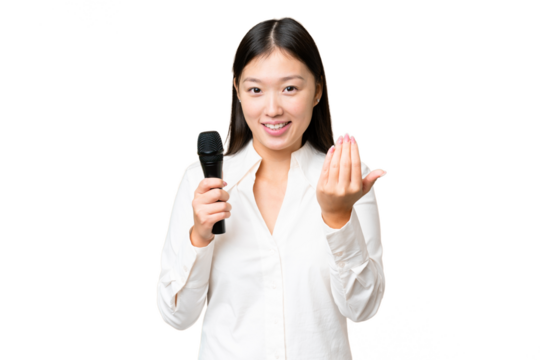Singer picking up a microphone over isolated chroma key background inviting to come with hand. Happy that you came