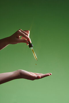 Female hand holding pipette dropper against green background