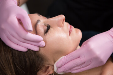Beautician in a beauty salon holds a cotton pad with which he cleans the face of a woman. Skin care and rejuvenation procedures.	