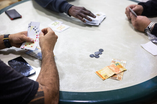 Three anonymous men playing card around round table and betting money