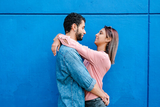 Engaged couple embracing in front of a blue wall
