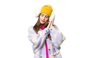 Young woman wearing winter muffs over isolated chroma key background making sleep gesture in dorable expression