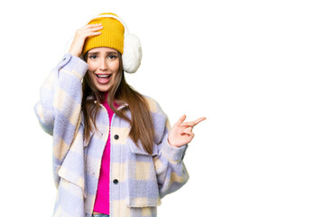 Young woman wearing winter muffs over isolated chroma key background surprised and pointing finger to the side