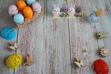 easter wooden background with colored eggs in a package, figures of fluffy bunnies in white and...