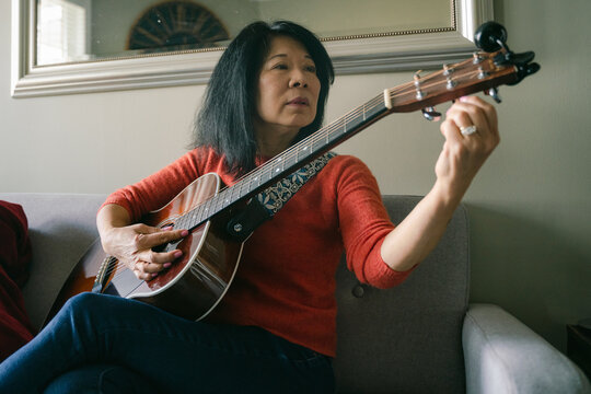 woman tuning guitar in her living room
