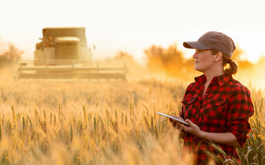 Woman farmer with digital tablet on a background of harvester. Smart farming concept.	