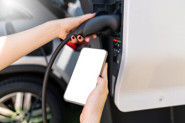 Hands with smartphone and charging plug on a background of electric car . White screen, you can add your content here	