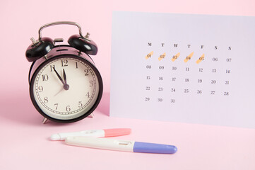Still life with positive pregnancy test kits, black alarm clock and white calendar with the dates...