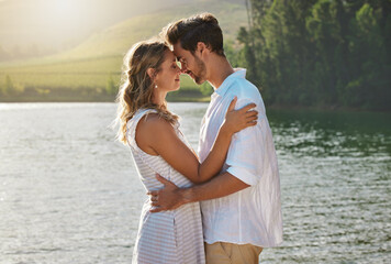 Couple, head touch and hug by lake for outdoor date, romantic adventure and summer love in nature....