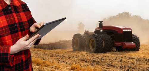 Farmer with digital tablet controls an autonomous tractor on a smart farm	