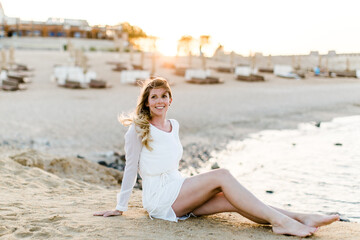 Frau im weißen Kleid sitzt am Strand