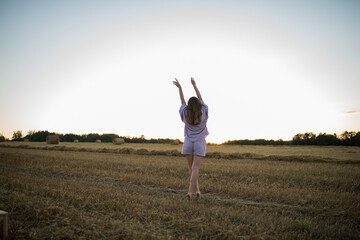 Fototapeta premium caucasian girl with long hair in a field at sunset looks into the distance, the concept of freedom, space and love for nature