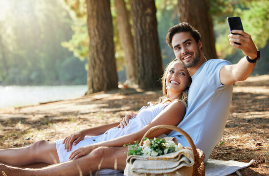 Couple, relax and smile for picnic selfie in the forest on holiday break or romantic summer vacation together. Happy man and woman relaxing or smiling on mat for photo, memory or date in nature