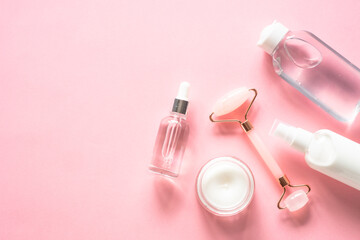 Fototapeta na wymiar Skin care concept. Jade roller, cream and serum bottle on pink. Flat lay image with copy space.