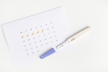 Flat lay. Positive pregnancy inkjet test and a calendar with the days of the last menstruation marked on white background. Women's health. Ovulation date calculation. Planning pregnancy and maternity