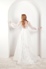 Fototapeta na wymiar From behind full length stylish bride irish redhead lady in white wedding dress posing at white wall. Fashionable pretty bride woman rear view. Fashion trendy style beauty concept. Copy ad text space