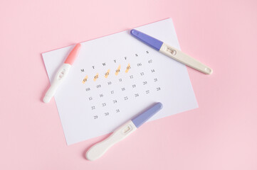 Flat lay Inkjet pregnancy test kits on a white calendar with marked dates in last menstruation, pink background. Calculation of ovulation day. Planning maternity. Gynecology and women's health concept