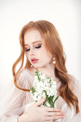 Portrait of bride irish lady in white wedding dress with red hair at white wall, closed eyes. Fashionable pretty woman with flowers bouquet. Fashion trendy style beauty concept. Copy ad text space