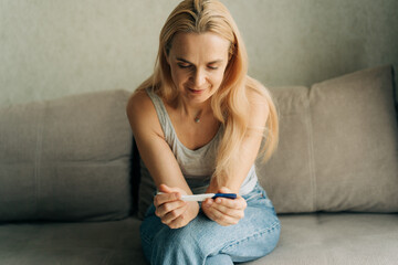 A woman in her forties sitting on a sofa holds a pregnancy test and waits for the result.