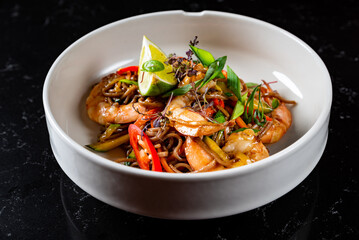 Stir fry noodles with vegetables and shrimps in plate on table background