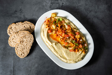 Dish of homemade chickpea hummus with olive oil, paprika, tomato, peppers, parsley, for vegans and vegetarians in a restaurant.