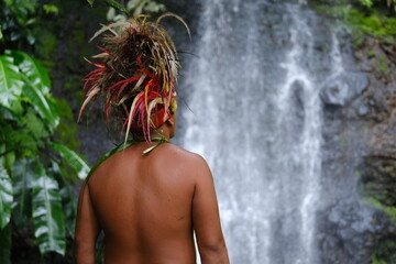 A Polynesian man from behind during a traditional ceremony with a waterfall in the background....