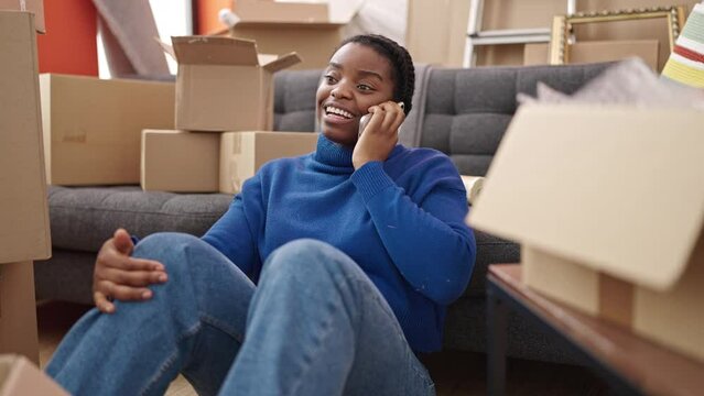 African american woman talking on smartphone sitting on floor at new home