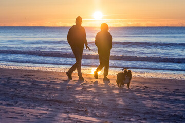 North Myrtle Beach, SC: Golden sun rising over the Atlantic Ocean with a man, woman, and dog...