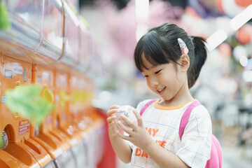 Cute young Asian girl smiling and happy after picking the toy out from Gachapon machine in mall,...