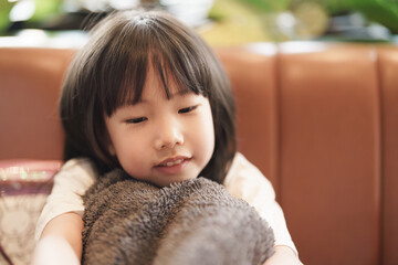 Cute Asian girl sitting at the sofa smiling feeling relax while hugging jacket, clam child, stay still, relax moment, thinking.