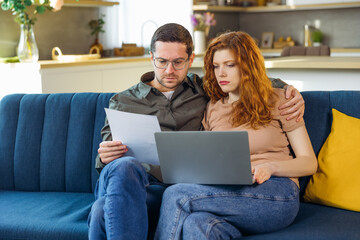 Shocked young couple receiving bad news, bankruptcy notice, reading letter, bank documents, confused wife and husband checking bills online, using laptop, financial problem