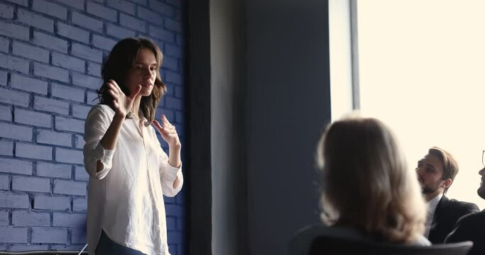 Engaged serious young corporate coach woman talking to colleagues on office meeting, gesturing, speaking, giving seminar. Team of business coworkers listening to presenter