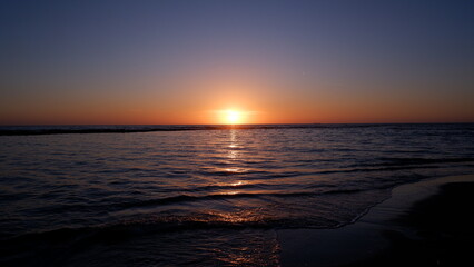Sunset on the sea in yellow, orange and blue colors, waves crashing on the beach.
