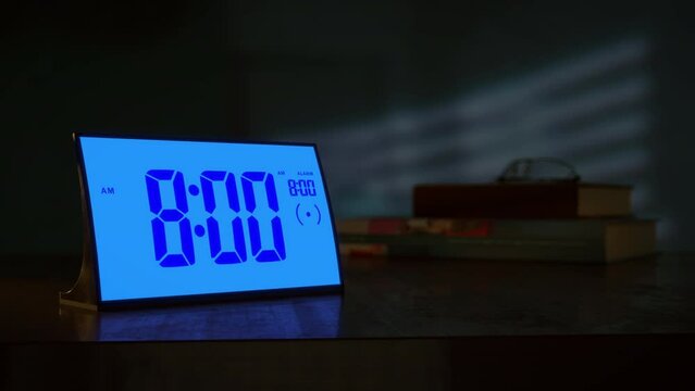 Digital alarm clock waking up at 8 AM. Close-up view. The numbers on the clock screen changes from 7:59 no 8:00 AM. Then alarm logo appears on the screen.	
