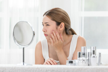 Asian young woman looking in mirror worry about pores facial skin problem with acne and dry skin....